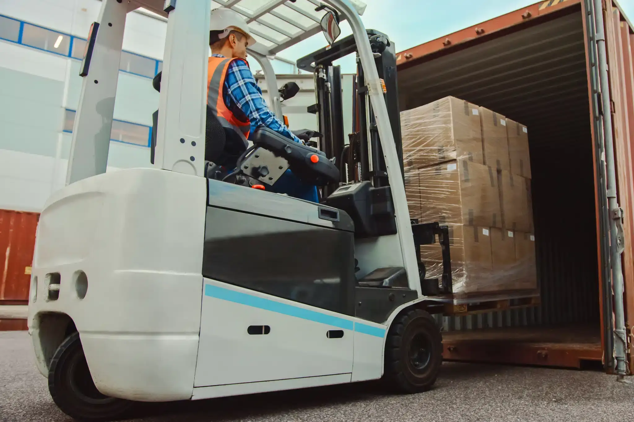 A worker using a forklift to load a pallet into a semi trailer